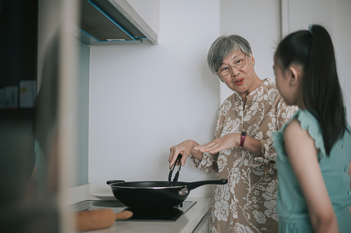Asian Chinese Senior woman cooking showing her granddaughter preparing Chinese dumpling in kitchen during weekend leisure time