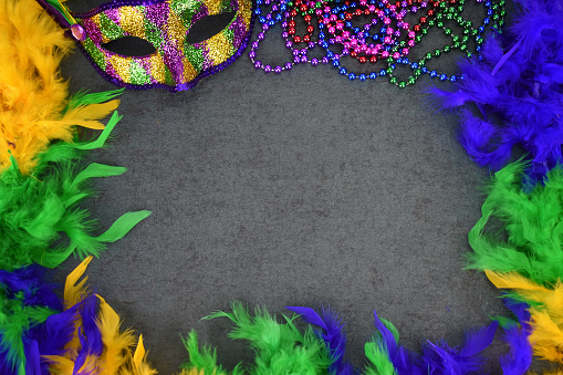 Festive Mardi Gras Celebration Carnival Mask, Feather Boa and Beads Border Over Blackboard Background with Copy Space