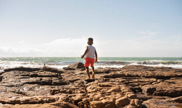 Little boy walking on some rocks by the ocean in summer