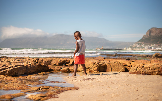 Rear view of a cute little African boy peeing into the ocean during a trip to the beach in the summertime