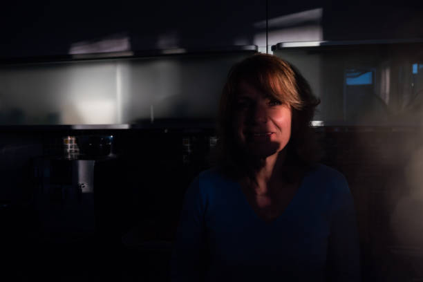 Portrait of woman with sunshine on face standing in dark kitchen.