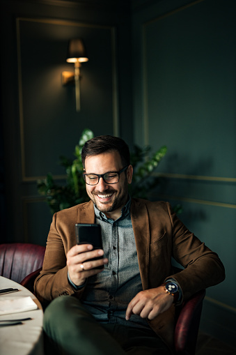 Cheerful handsome businessman using smart phone at restaurant, portrait.