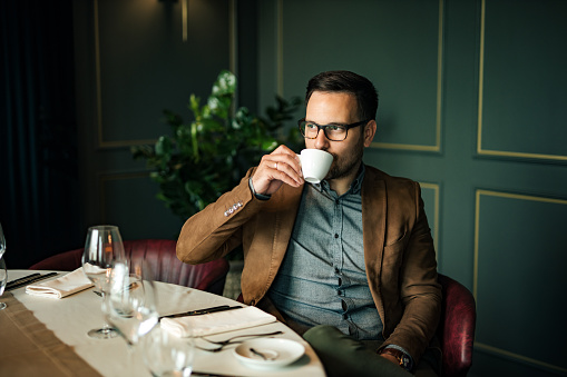 Portrait of elegant man drinking cup of coffee at fancy restaurant.