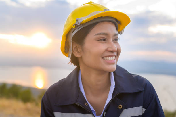 a woman engineer is putting a protective helmet on her head at sunset.
