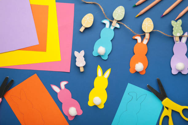 istock Easter bunnies handmade from colored paper, easy crafts for kids on a blue background. 1365874612
