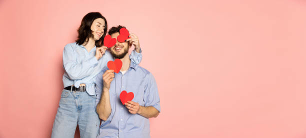 flyer. young and happy man and woman holding greeting cards shaped hearts isolated on pink trendy color background. emotions, youth, love and lifestyle concept - valentijn stockfoto's en -beelden