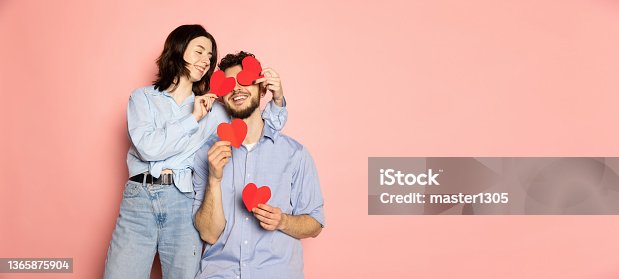 istock Flyer. Young and happy man and woman holding greeting cards shaped hearts isolated on pink trendy color background. Emotions, youth, love and lifestyle concept 1365875904