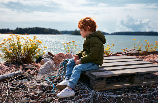cute redhead kid sitting on wooden pallet in front of the Baltic sea and tansy flowers