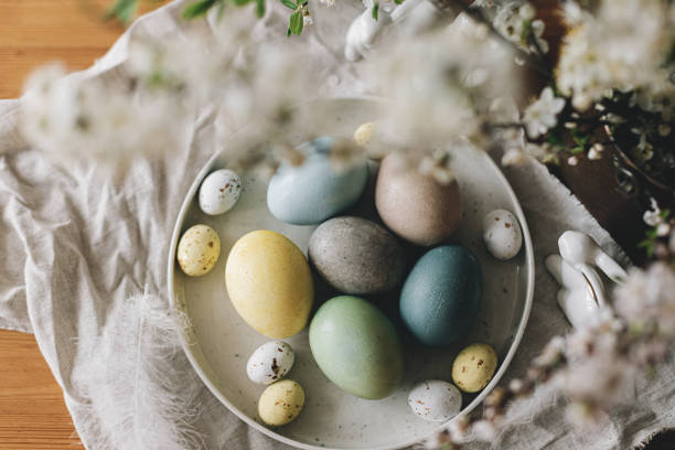 istock Happy Easter! Easter eggs on plate with bunny figurines, linen napkin,  cherry blossoms on rustic table. Natural dyed colorful eggs and spring flowers. Countryside still life, top view 1365876245