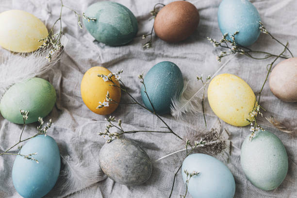 istock Easter eggs on rustic linen napkin with tender flowers. Happy Easter! Stylish natural dyed pastel colorful egg, spring flowers and feathers composition. Rustic still life top view 1365878673