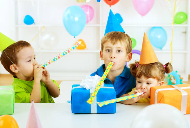 Group of cheerful children having fun playing at an outdoor playground birthday party, doing egg and spoon balance race