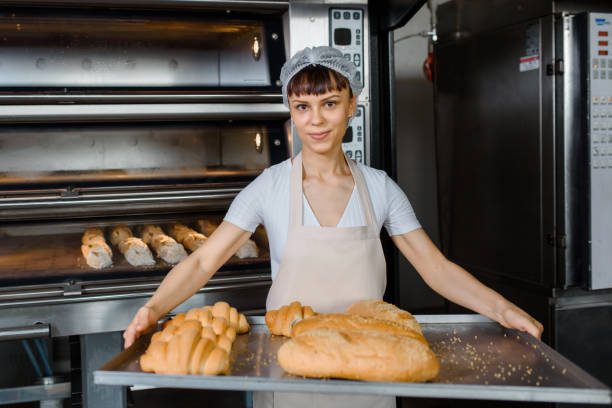 istock Baker is holding a tray with fresh bread in a bakery bread factory 1365882365