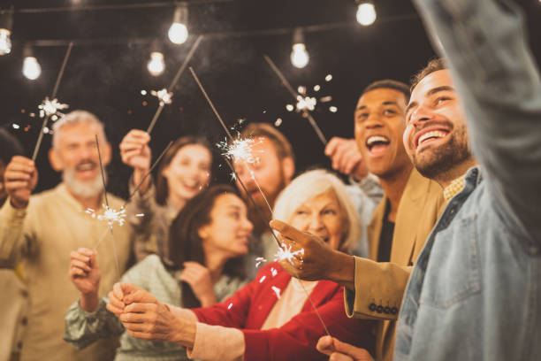 Family and friends celebrating at dinner on a rooftop terrace multiethnic group of people dining on a rooftop, people celebrating with fireworks. Family and friends make a reunion at home, eating and having fun reunion stock pictures, royalty-free photos & images