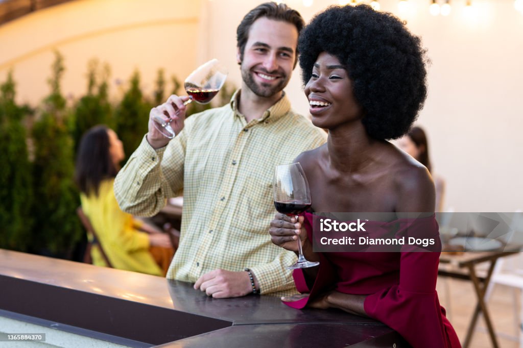Family and friends celebrating at dinner on a rooftop terrace multiethnic group of people dining on a rooftop. Family and friends make a reunion at home, eating and having fun Wine Stock Photo