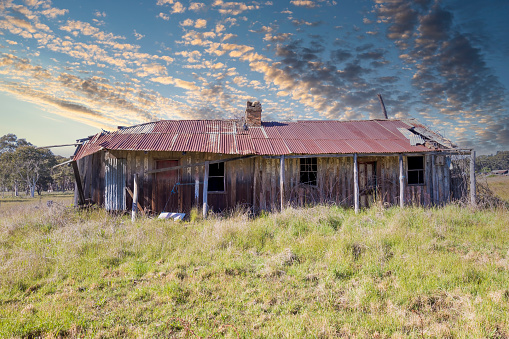 Photograph of an old and rusted out and broken down wooden residential building in the middle of a green agricultural field