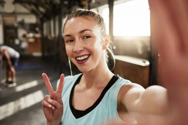 Photo of Shot of a young woman showing the peace sign while at the gym