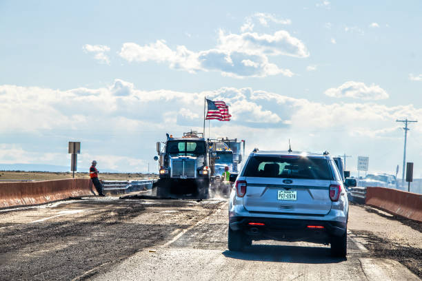 retraso del tráfico con la construcción de carreteras con trabajadores y camiones con enorme bandera estadounidense y polvo y automóvil de texas en primer plano esperando - editorial land vehicle construction equipment built structure fotografías e imágenes de stock