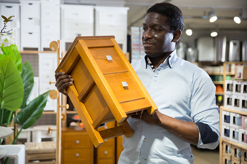 African american male shopper looking with interest at small bedside cabinet with drawers in home decor store