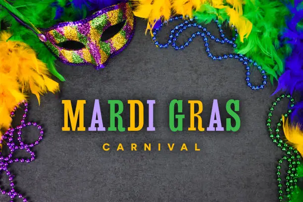 Photo of Mardi Gras Carnival Greeting Card Design with Colorful Text Illustration, Masquerade Party Mask, Feather Boa and Beads Over Black Background Texture