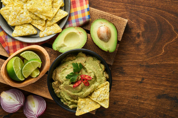 Guacamole. Traditional latinamerican Mexican dip sauce in a black bowl with avocado and ingredients and corn nachos. Avocado spread. Top view. Copyspace stock photo