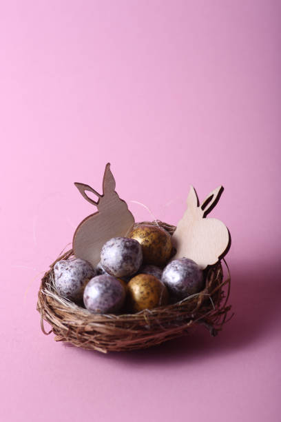 istock Easter concept - two rabbits in a nest with chocolate eggs against pink background 1365893327