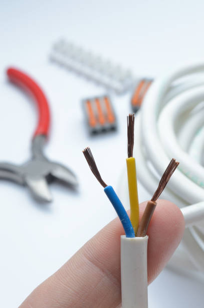 istock stripped, electrical three-core wire in hand against the background of terminal blocks and tools. close-up. 1365895048