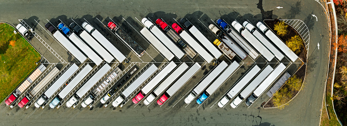 Stitched panoramic drone shot looking straight down on a line of diagonally parked trucks at a truck stop in Stamford, Connecticut on a sunny day in Fall.