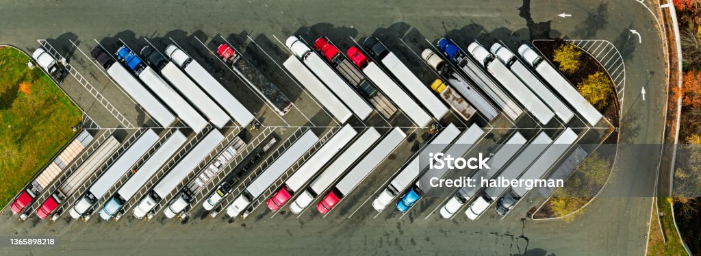 Panoramic Top Down Drone Shot of Trucks Parked at Truck Stop Stitched panoramic drone shot looking straight down on a line of diagonally parked trucks at a truck stop in Stamford, Connecticut on a sunny day in Fall. Semi-Truck Stock Photo