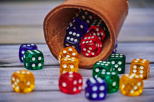 View to different colored game dices and a dice cup on a wooden table.