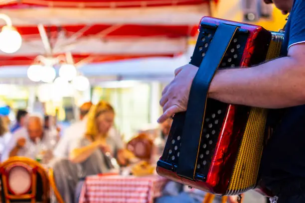 An accordion player musician plays for diners at an outdoor Italian restaurant in the center of Old Town Nice, France.