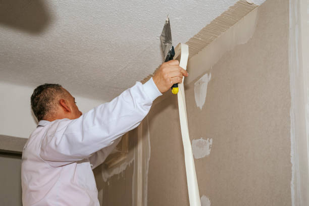 Man working on drywall or plaster putting drywall mesh tape on a wall using a putty knife and plaster. stock photo