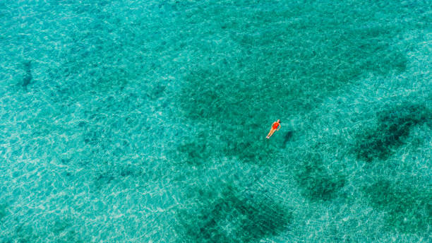 Aerial view of female in red swimsuit swimming in the turquoise sea of Albania stock photo