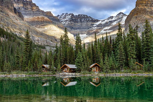 Lake O'Hara cabins reflecting in the emerald water of the lake with mountain peaks in the background, Yoho National Park, Canada.