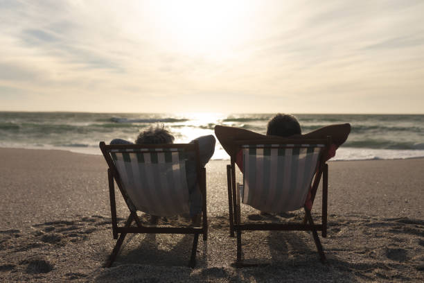istock Retired senior multiracial couple relaxing while sitting on folding chairs looking sea from beach 1365904943