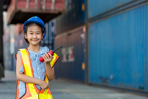 Asian little girl  holding walkie- talkie at Container cargo site. Business heir concept.