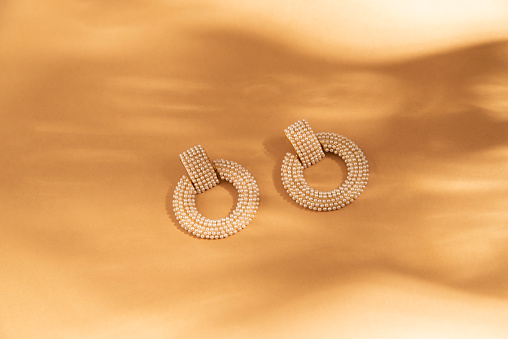 Fashionable gold handmade earrings on a beige background. Flat lay, top view, minimalist fashion jewelry with shadows of sunlight