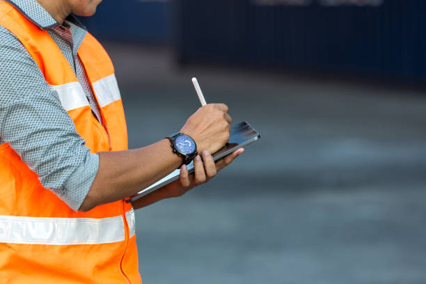 Foreman or worker hand holding tablet for writing and checking in goods in container at Container cargo site. stock photo