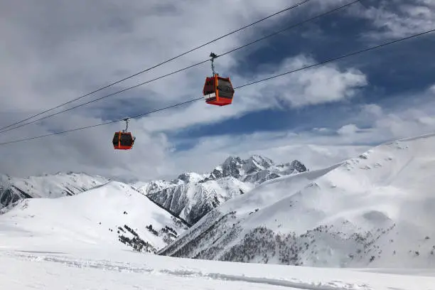 Two red gondolas on sky and cloudly background lift people in high mountains. Active winter leasure concept.