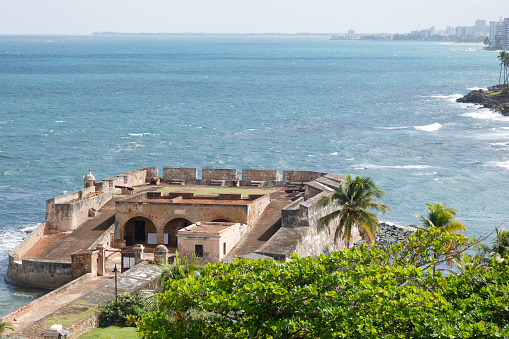 Fortín de San Gerónimo de Boquerón is a small fort located at the mouth of the Condado Lagoon, across from the historic sector of Miramar in San Juan, Puerto Rico.  This is a view from an elevated angle.  You can see the ocean and the skyline of San Juan in the background.  There are palm and other tropical trees in the foreground.