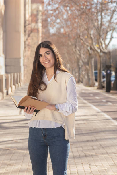 istock Student girl smiling while looking at camera. Young lady with a notebook in her hand on the university campus. 1365906721