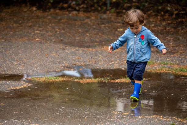 istock Little boy with blue rubber boots crossing a puddle in a rainy day 1365908646