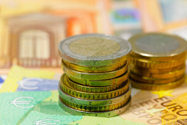 istock Coins stacked in two piles on banknotes, EUR currency. 1365910942