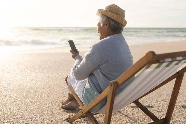 istock Biracial senior woman using smartphone for video call while sitting on chair at beach during sunset 1365911193