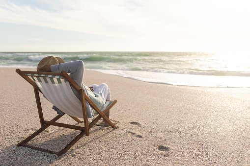 Relaxed retired senior biracial woman sitting on folding chair enjoying sunset at beach. lifestyle and weekend.
