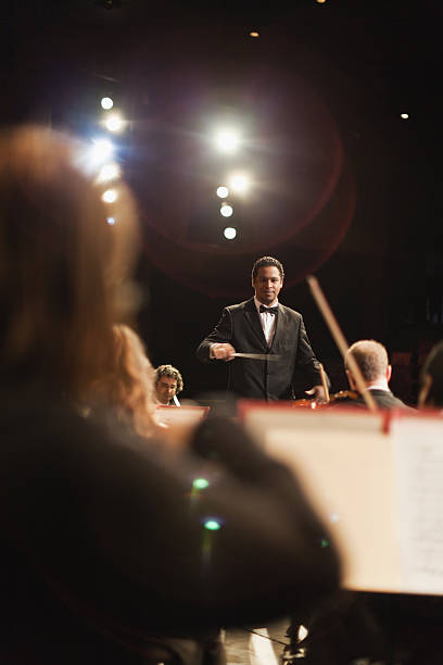 Conductor waving baton over orchestra  musical conductor stock pictures, royalty-free photos & images
