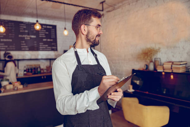 istock Joyful male worker writing on clipboard in cafe 1365920032