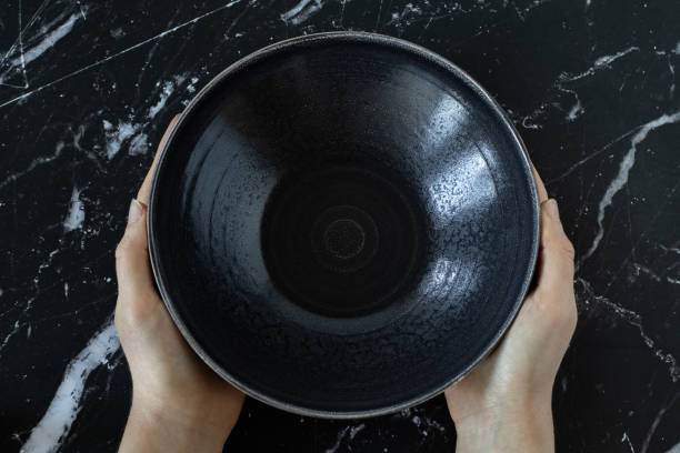 Woman's hands holding an empty dish bowl on a black textured table fasting biblical concept stock photo