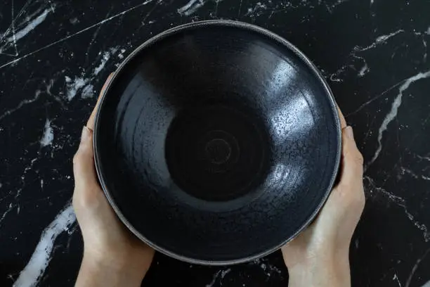 Fasting Christian biblical concept. Woman's hands holding an empty dish bowl on a black textured table. Spiritual fast for forgiveness, repentance, and relationship with God Jesus Christ.