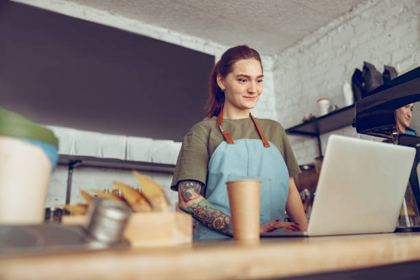 istock Smiling young woman barista using notebook in coffee shop 1365921850