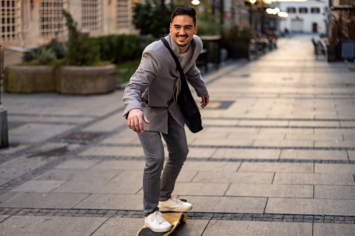 Calm businessman with briefcase in hand riding on skateboard at street, looking away